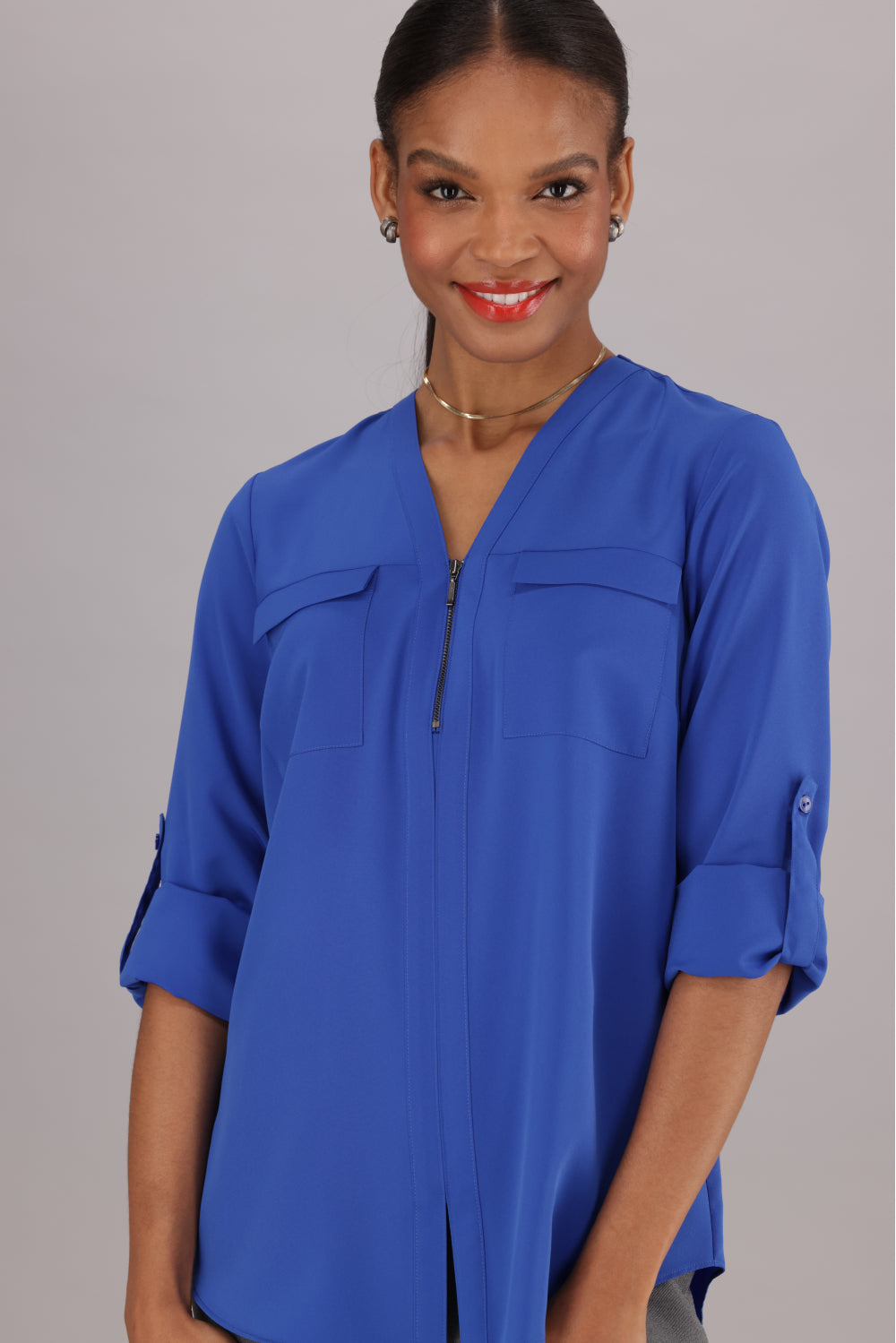 A Bright Blue Women's Blouse with a Zip-up Front and Two-Pocket detail. and Roll-Up Tab sleeves.